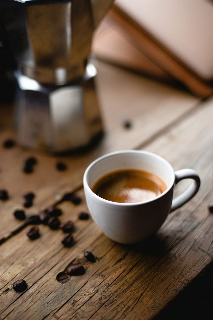 Una tazzina di caffè su un tavolo di legno, con la moka sullo sfondo.
